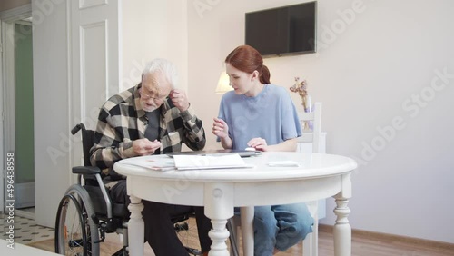 Old man learning how to use wireless headphones. His granddaughter helps him turn on music from the computer photo