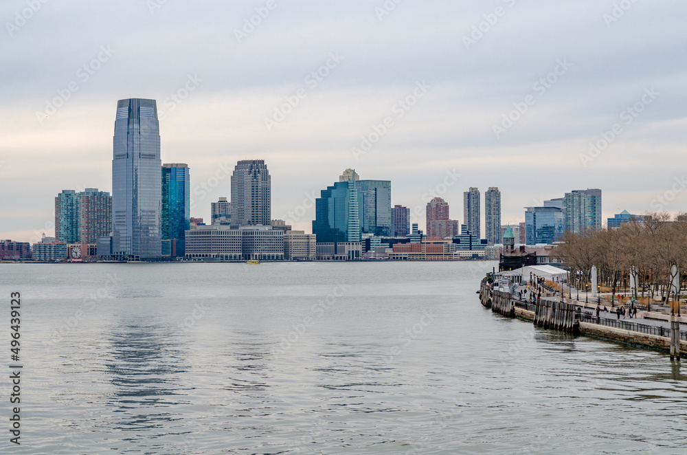 Fototapeta premium Jersey City, New Jersey with office skyscraper, Hudson river and Manhattan river bank in forefront, during winter evening with overcast, horizontal