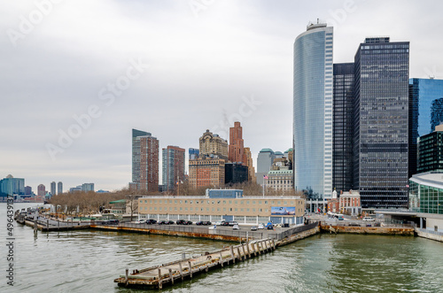 Manhattan with Battery Park, wood jetty and Hudson river in the forefront, during winter evening with overcast, horizontal © Bildgigant