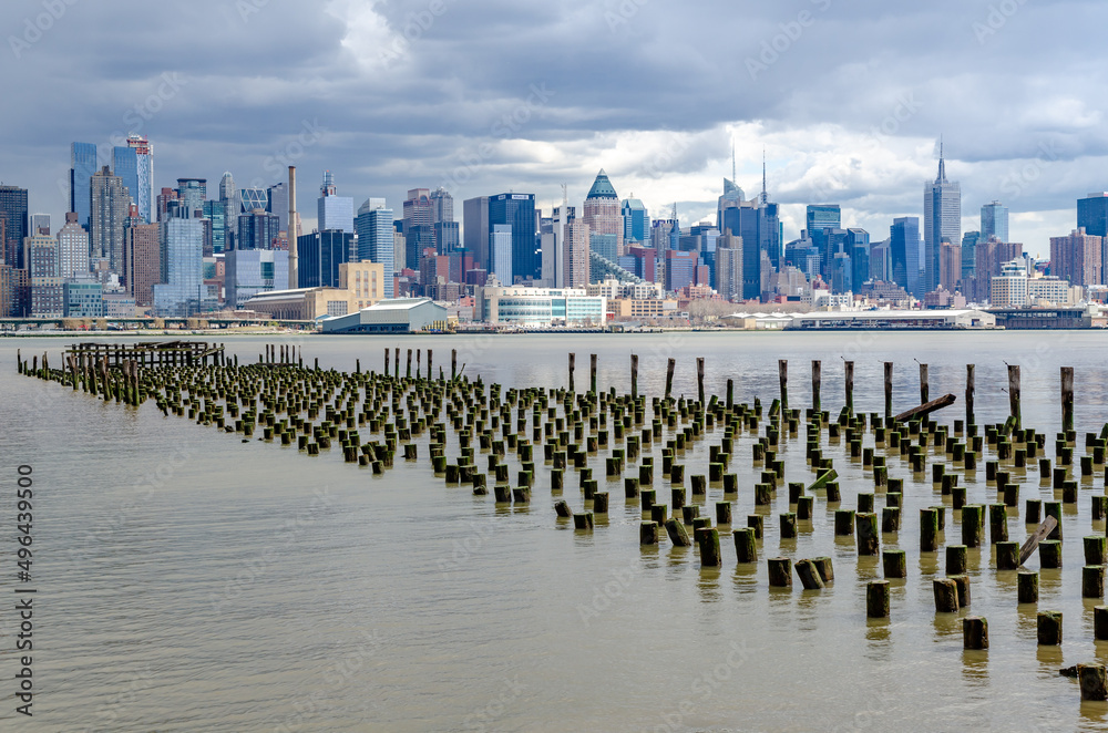 View of Manhattan Skyline, New York City with Hudson river and old wooden landing stage in front during cloudy winter day, vertical