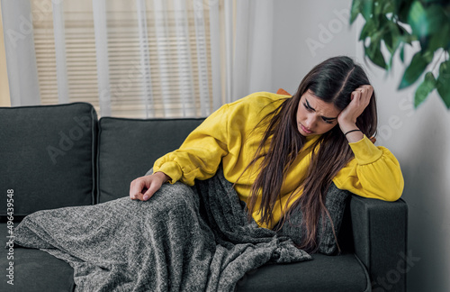 Tired caucasian girl, covered with blanket, laying on sofa.