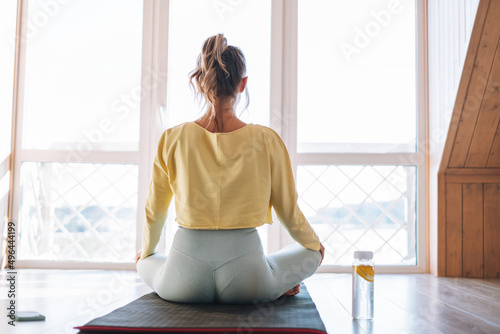 Young sllim fitness blonde woman practice morning yoga near window of home