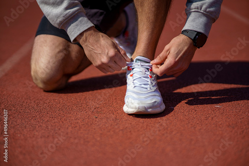 Runner man tying shoelace in the stadium  cross training workout. Sporty male training outside