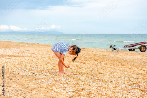 little charming girl 5-7 years old in a striped t-shirt happily plays on the beach on a sunny day on vacation 