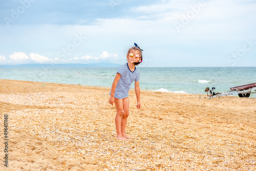 little charming girl 5-7 years old in a striped t-shirt happily plays on the beach on a sunny day on vacation 