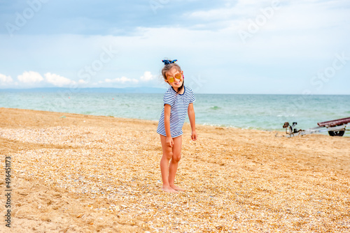 little charming girl 5-7 years old in a striped t-shirt happily plays on the beach on a sunny day on vacation 