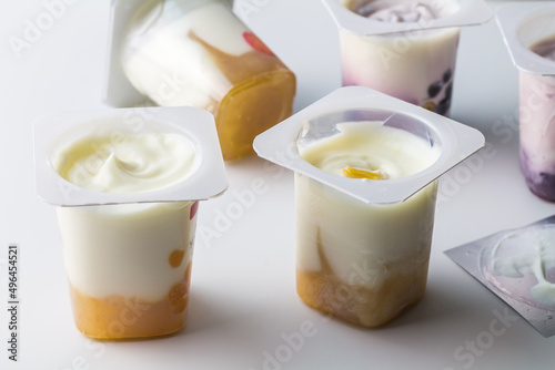 Fruit flavoured yogurt in transparent plastic cups on white background with silver foil lid - Yoghurt cups background with selective focus