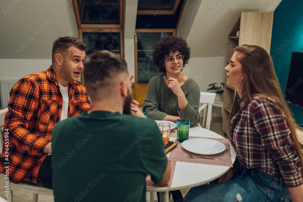 Group of friends enjoying dinner while sitting at the kitchen table together Group of friends enjoying dinner while sitting at the kitchen table together