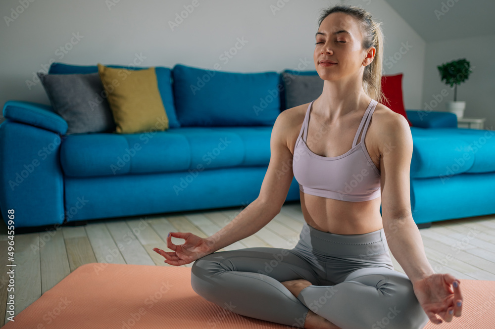 Woman siting in a lotus yoga position on the fitness mat at home Woman siting in a lotus yoga position on the fitness mat at home