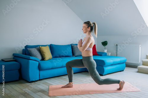 Woman training yoga at home an standing in warrior one pose.