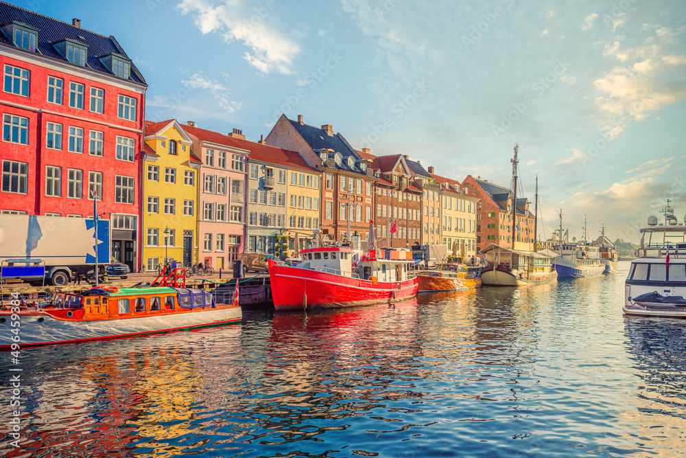 Obraz premium An old red and white fishing boat stands among other ships and yachts near the old small multi-colored houses in the Nyhavn canal. Copenhagen, Denmark