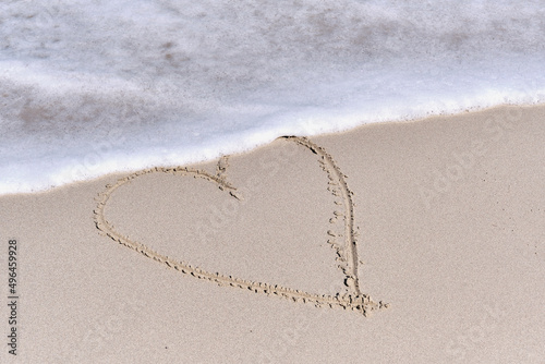 Contour of heart drawn on white sand of tropical beach.