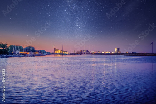 Sea bay with yachts, factory pipes and a processing factory against the background of the night sky and the stars of the milky way. Copenhagen, Denmark
