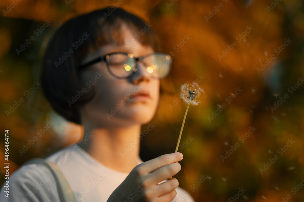 A girl blowing dandelion seeds. The white dandelion is flying. Portrait of a teenage girl with glasses A girl blowing dandelion seeds. The white dandelion is flying. Portrait of a teenage girl with glasses