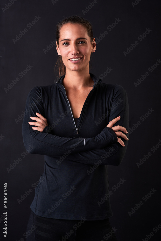 Feeling good and looking great. Studio portrait of a young woman in gym clothes standing with her arms crossed against a dark background.