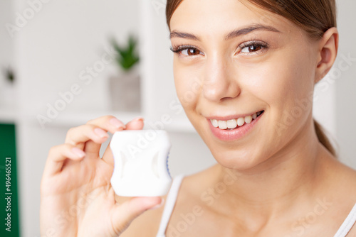 Portrait of cheerful girl using special thread for cleaning teeth.
