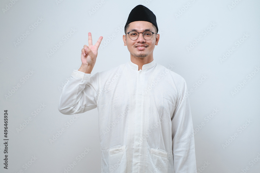 Asian muslim man wearing casual clothes showing and pointing up with fingers number two while smiling confident and happy Asian muslim man wearing casual clothes showing and pointing up with fingers number two while smiling confident and happy