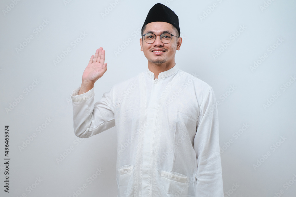 Asian muslim man smiling at camera while waving hand say hello Asian muslim man smiling at camera while waving hand say hello