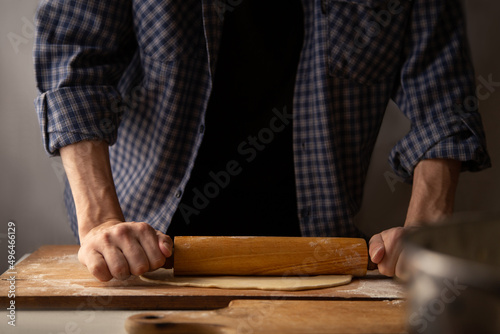 Dough rolling process. A man in a plaid shirt uses a rolling pin to roll out dough for making dumplings.