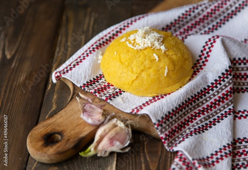 Traditional Moldovan cuisine. Hominy with cheese on a Moldovan towel and a wooden board and garlic on a dark background