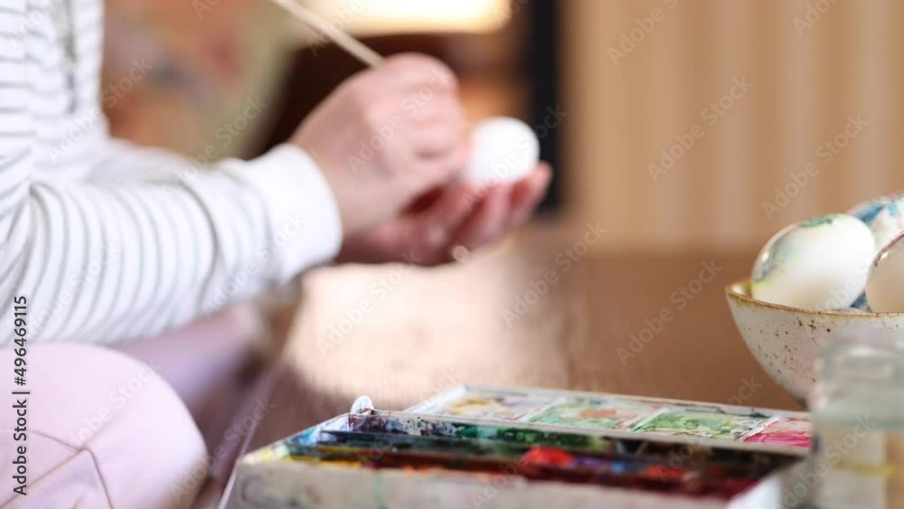 Defocused process of woman paiting a water colors on fantasy chicken eggs. Female preparing for Easter egg festival. Focus on table with print Defocused process of woman paiting a water colors on fantasy chicken eggs. Female preparing for Easter egg festival. Focus on table with print