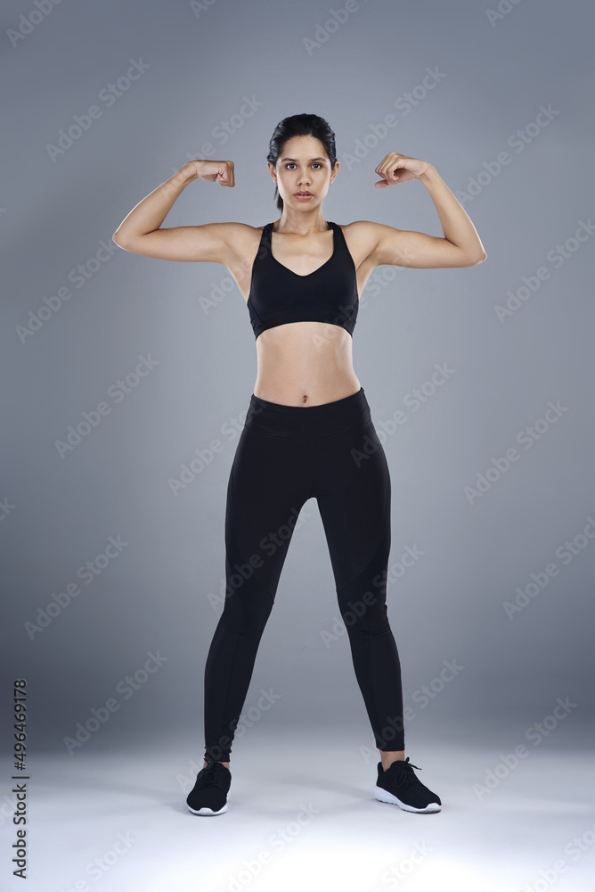 Inner strength is the greatest form of strength to have. Full length shot of a sporty young woman flexing her biceps against a grey background. Inner strength is the greatest form of strength to have. Full length shot of a sporty young woman flexing her biceps against a grey background.