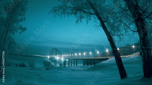 in the early morning a blizzard with snow sweeps and the sun slowly illuminates the transport bridge in siberia