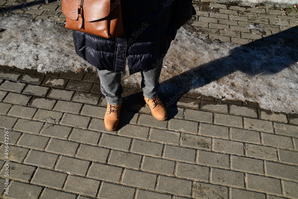 A woman stands on a paving slab freed from snow. Early spring in the city.