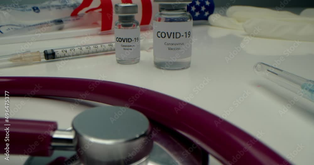Vaccine against COVID-19, an ampoule with a vaccine against coronavirus and various syringes nearby, medical instruments,protective mask have been developed, background of the American flag and books Vaccine against COVID-19, an ampoule with a vaccine against coronavirus and various syringes nearby, medical instruments,protective mask have been developed, background of the American flag and books