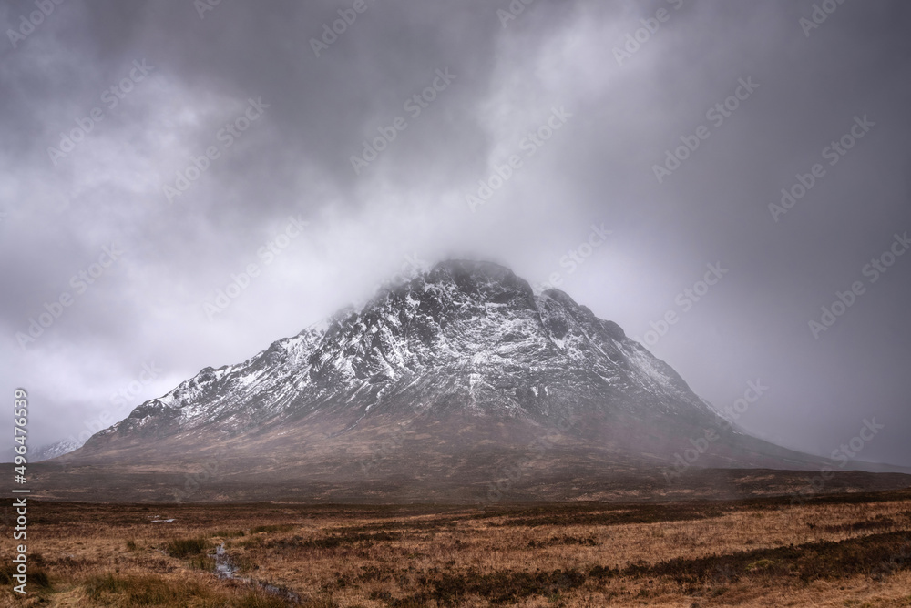 Beautiful Winter landscape image of Stob Dearg Buachaille Etive Mor viewed from Rannoch Moor with snowcapped peak and beautiful moody cloud formations