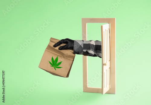 Concept of marijuana delivery. Courier's hand with  package of medical marijuana is stretched out of open door on  green background. Minimal art poster.