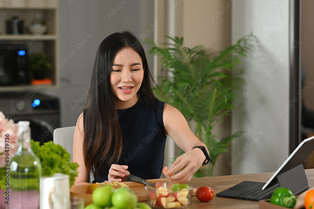 A portrait of a young pretty Asian woman chopping fruits and preparing a meal on a wooden cut board, for food, health and cooking concept.
