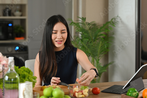 A portrait of a young pretty Asian woman chopping fruits and preparing a meal on a wooden cut board  for food  health and cooking concept.