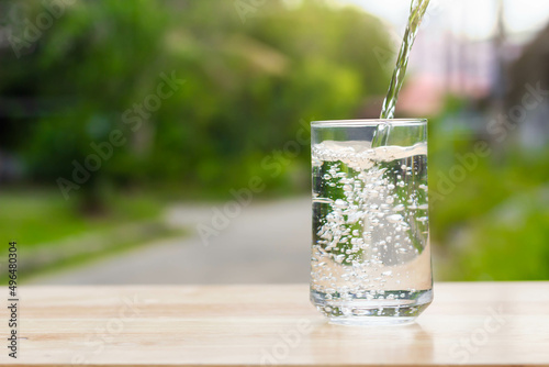 Pour water into glass on wooden table outdoors and green background.