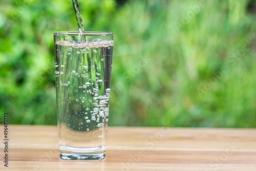 Pour water into glass on wooden table outdoors and green background.