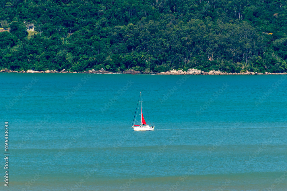 Obraz premium Boat sailing on the blue sea of Balneário Camboriú Brazil with a forest in the background.