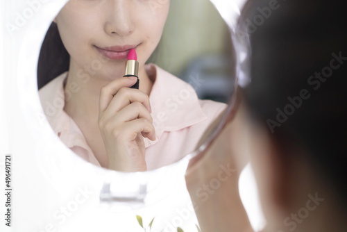 Young woman applying lipstick in mirror