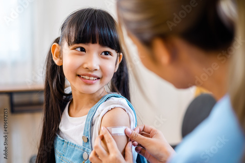 Childhood vaccination. Asian young woman doctor vaccinating little girl at home. Vaccine for covid-19 coronavirus, flu, infectious diseases.