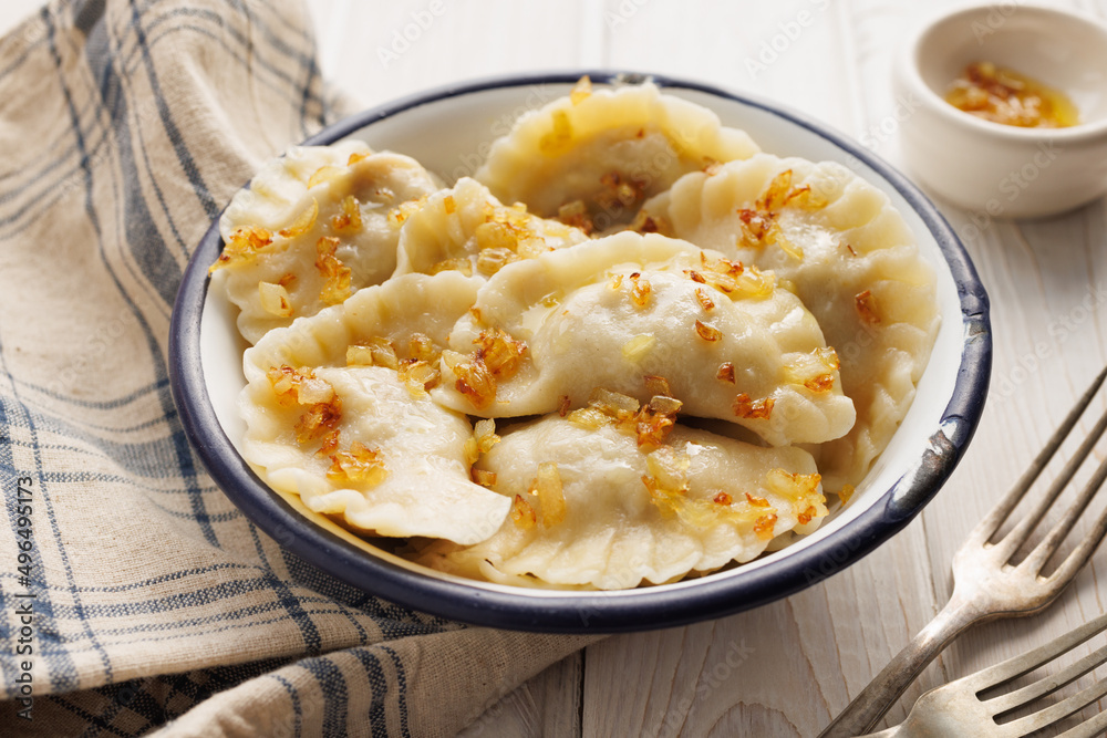 Homemade dumplings with the addition of fried chopped onion in a bowl on a wooden table, close up view. Traditional food