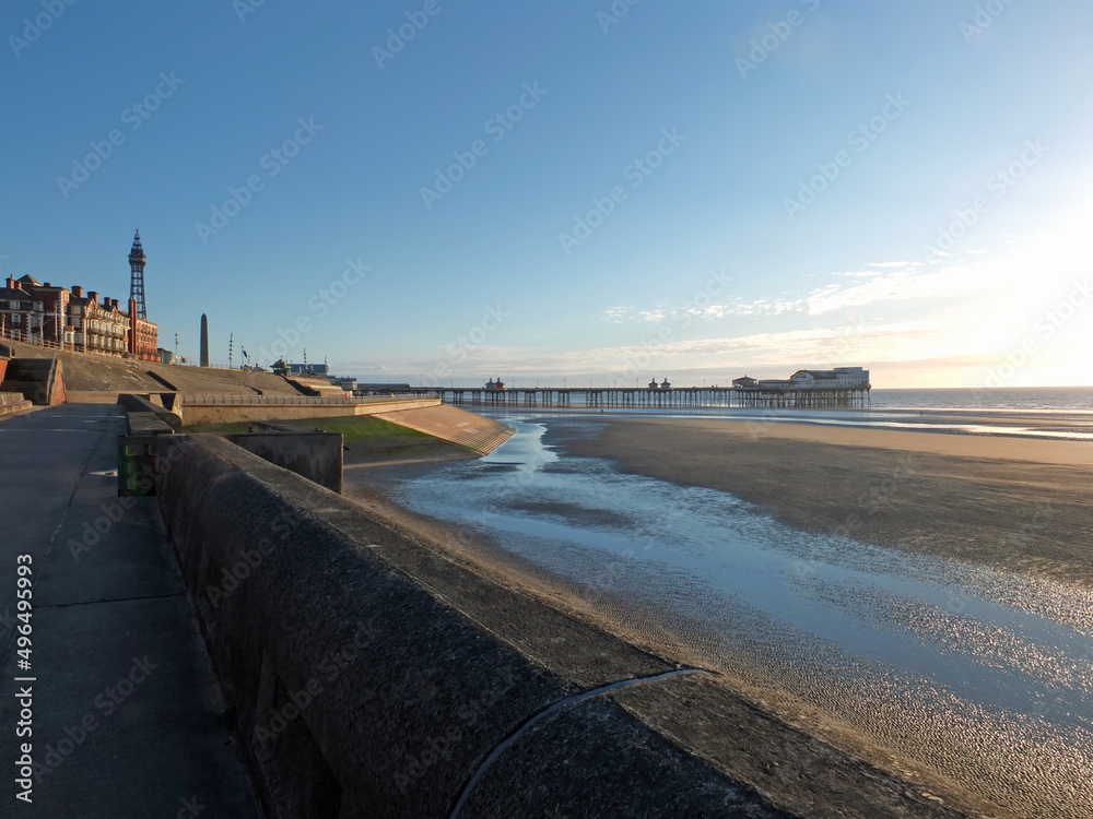 view of blackpool tower and south pier from the promenade with town buildings in afternoon sunlight