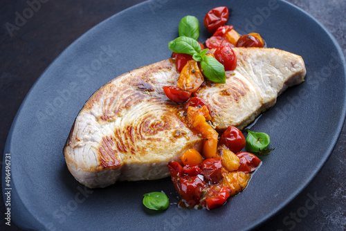 Fried swordfish steak with tomatoes and paprika served as close-up on a design plate photo