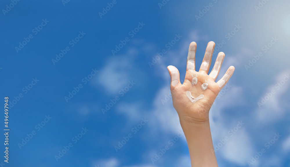 Positive symbol drawing by sunscreen (sun cream, suntan lotion) on caucasian open hand on blue sky background. Concept of protection from sun, skin care, happy summer vacation. Copy space. Positive symbol drawing by sunscreen (sun cream, suntan lotion) on caucasian open hand on blue sky background. Concept of protection from sun, skin care, happy summer vacation. Copy space.