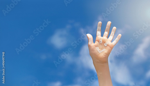 Positive symbol drawing by sunscreen (sun cream, suntan lotion) on caucasian open hand on blue sky background. Concept of protection from sun, skin care, happy summer vacation. Copy space.