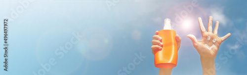Banner of positive symbol drawing by sunscreen on open hand, another hand holding a bottle of suntan lotion. Two hands on blue sky, clouds, beams of sun background.