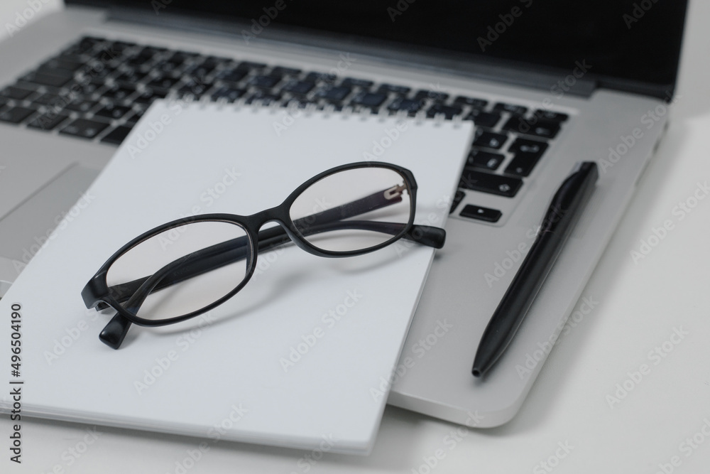 Desk with laptop, notebook, glasses and pen close-up. Work from home or office concept Desk with laptop, notebook, glasses and pen close-up. Work from home or office concept