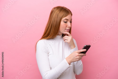 Young redhead woman isolated on pink background thinking and sending a message