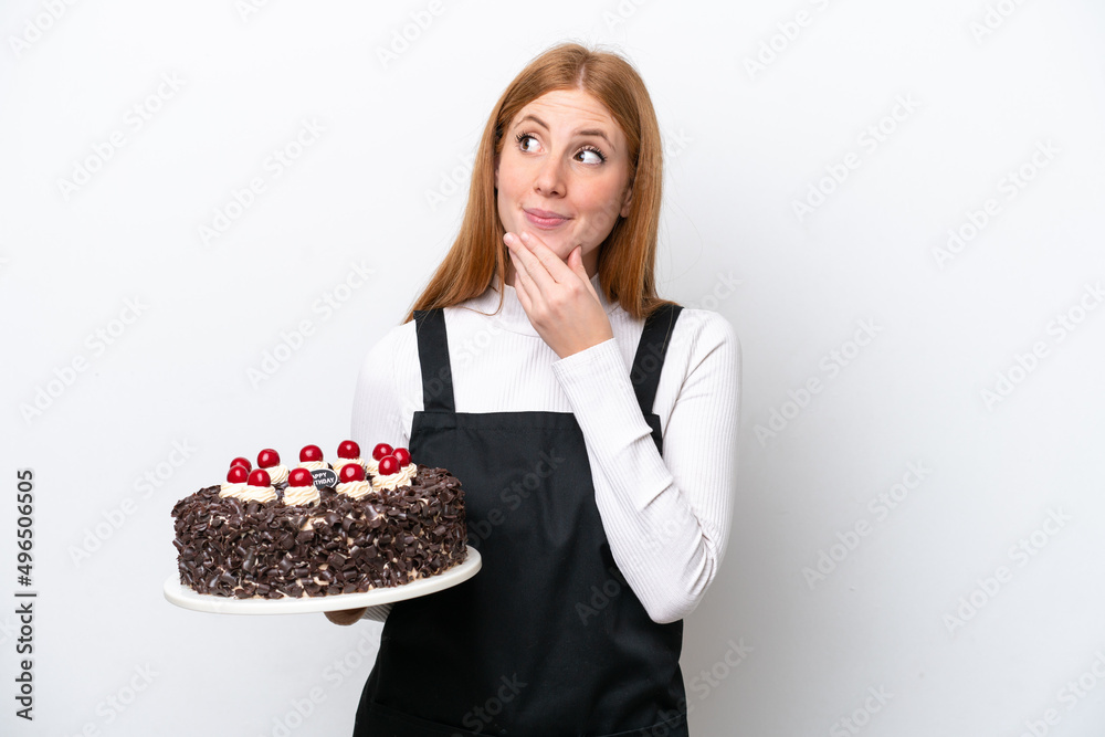 Young redhead woman holding birthday cake isolated on white background looking up while smiling Young redhead woman holding birthday cake isolated on white background looking up while smiling