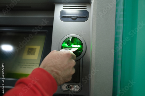 ATM, a man who puts his card in an ATM, green card slot and an automatic teller, qr code and other operations section standing on the screen photo