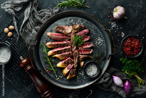 Chopped juicy porterhouse steak or T Bone Steak dry aged of beef Ready to Cook on wooden Board with herbs, pepper and salt. On a black stone background.