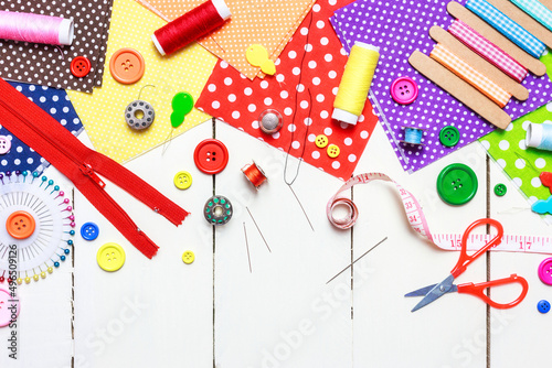 Various fabric, sewing tools and buttons on a white wooden table